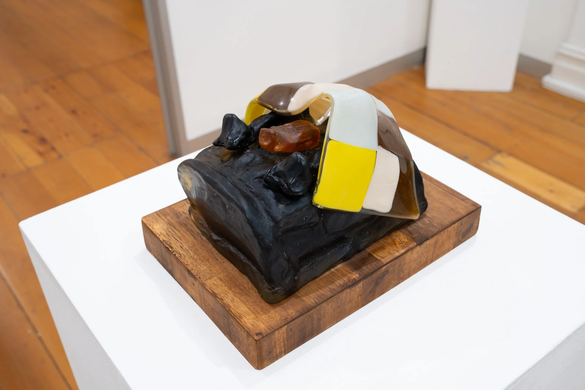 Close up of a small glass and wood sculpture on a white plinth