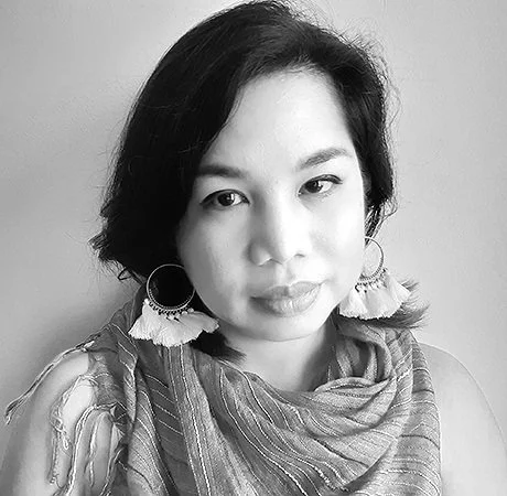 Black and white portrait of a person with short dark hair, wearing large hoop earrings with tassels, and a textured scarf.