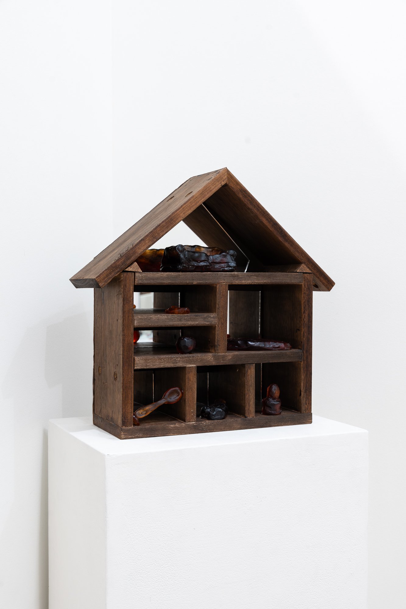 Image of wooden house artwork with glass objects in it in a white gallery space 