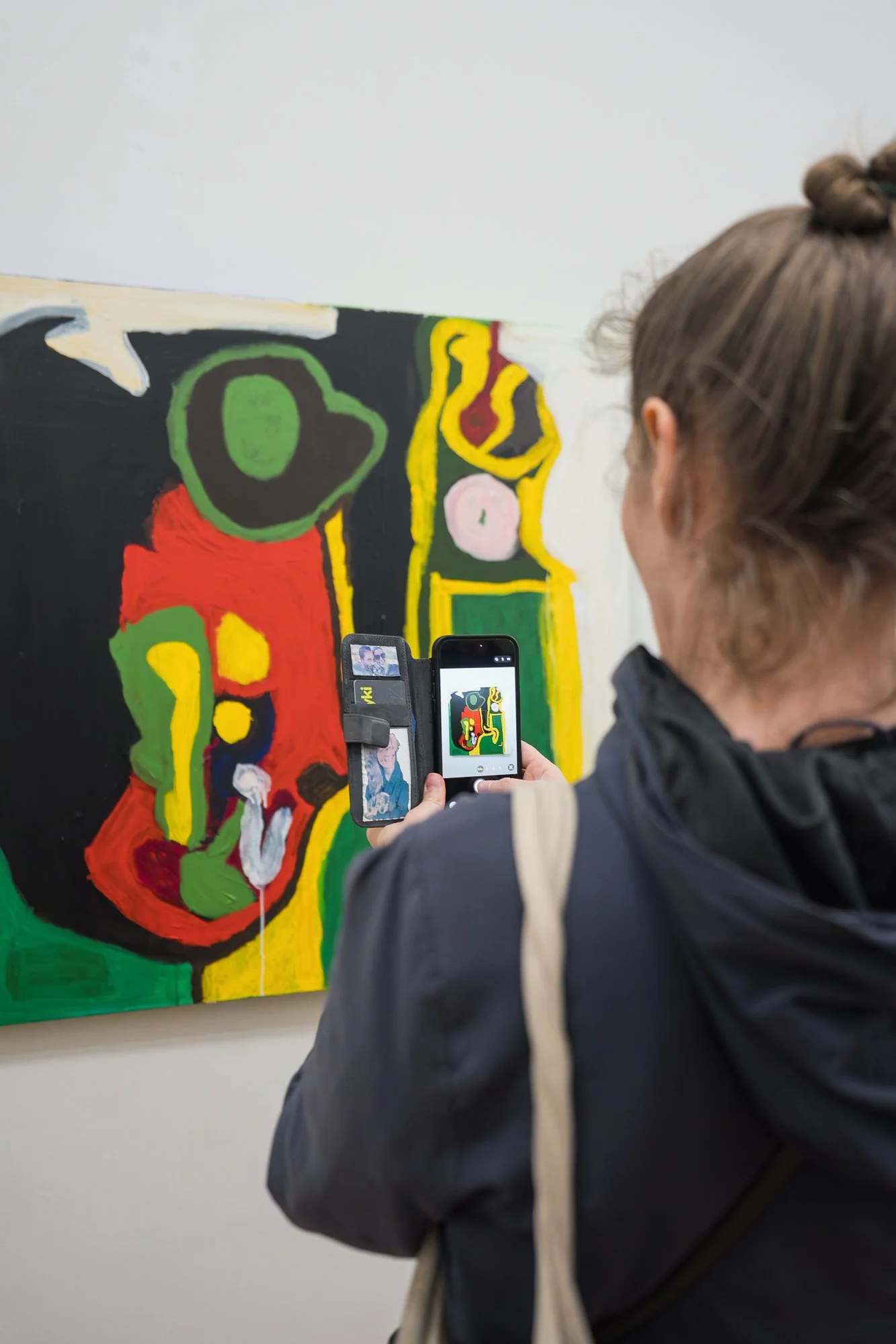 A visitor photographs a large, bold abstract painting in greens, reds and yellows on her phone.