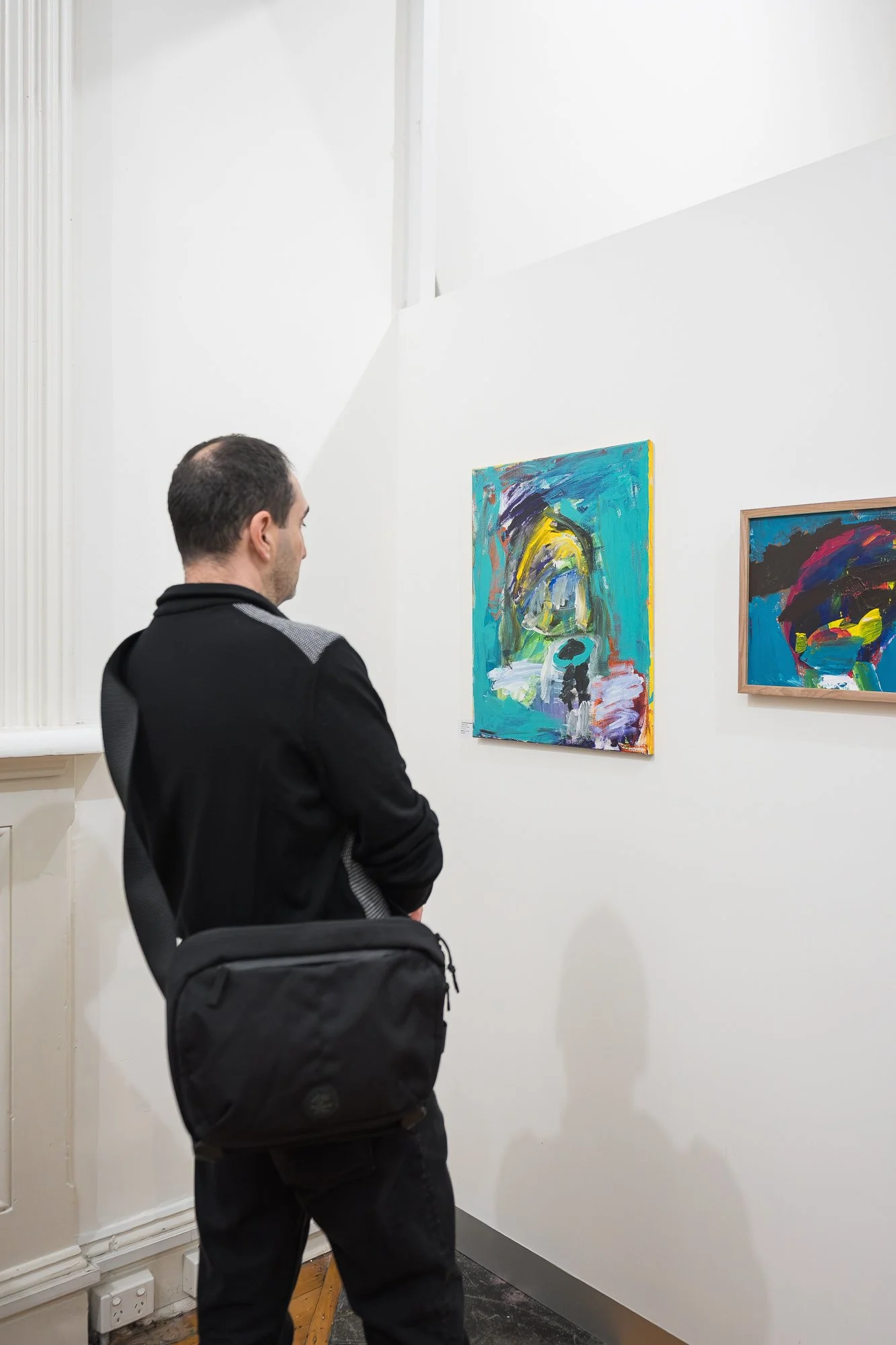 A visitor in black stands quietly before two bold abstract paintings in teal and deep blue.