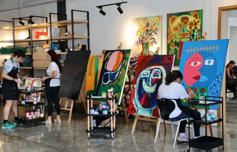 View of a busy studio space, with two staff and a seated artist working on a painting.