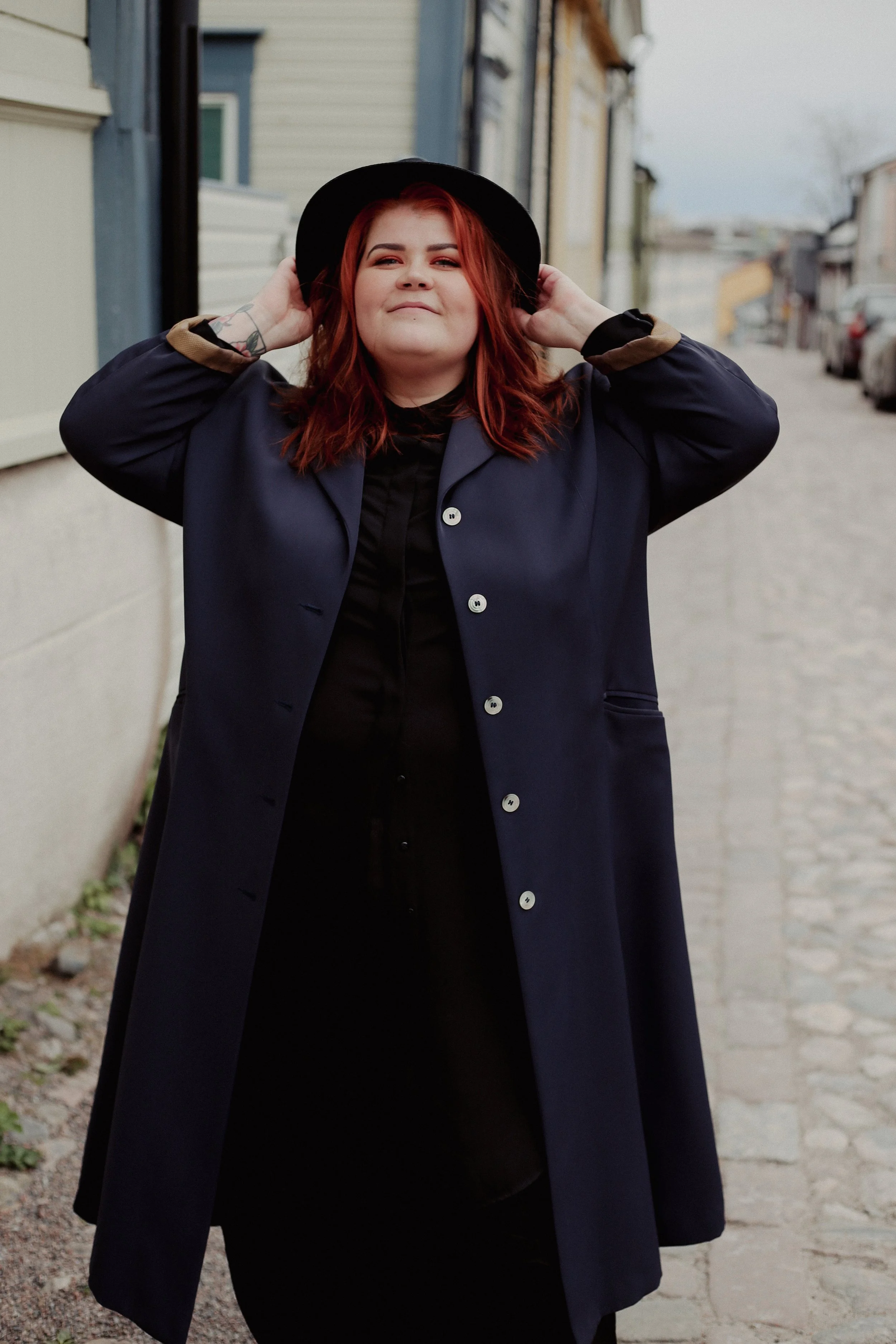 Verkkosivusuunnittelija seisoo kadulla ja pitelee hymyillen kiinni hatustaan.