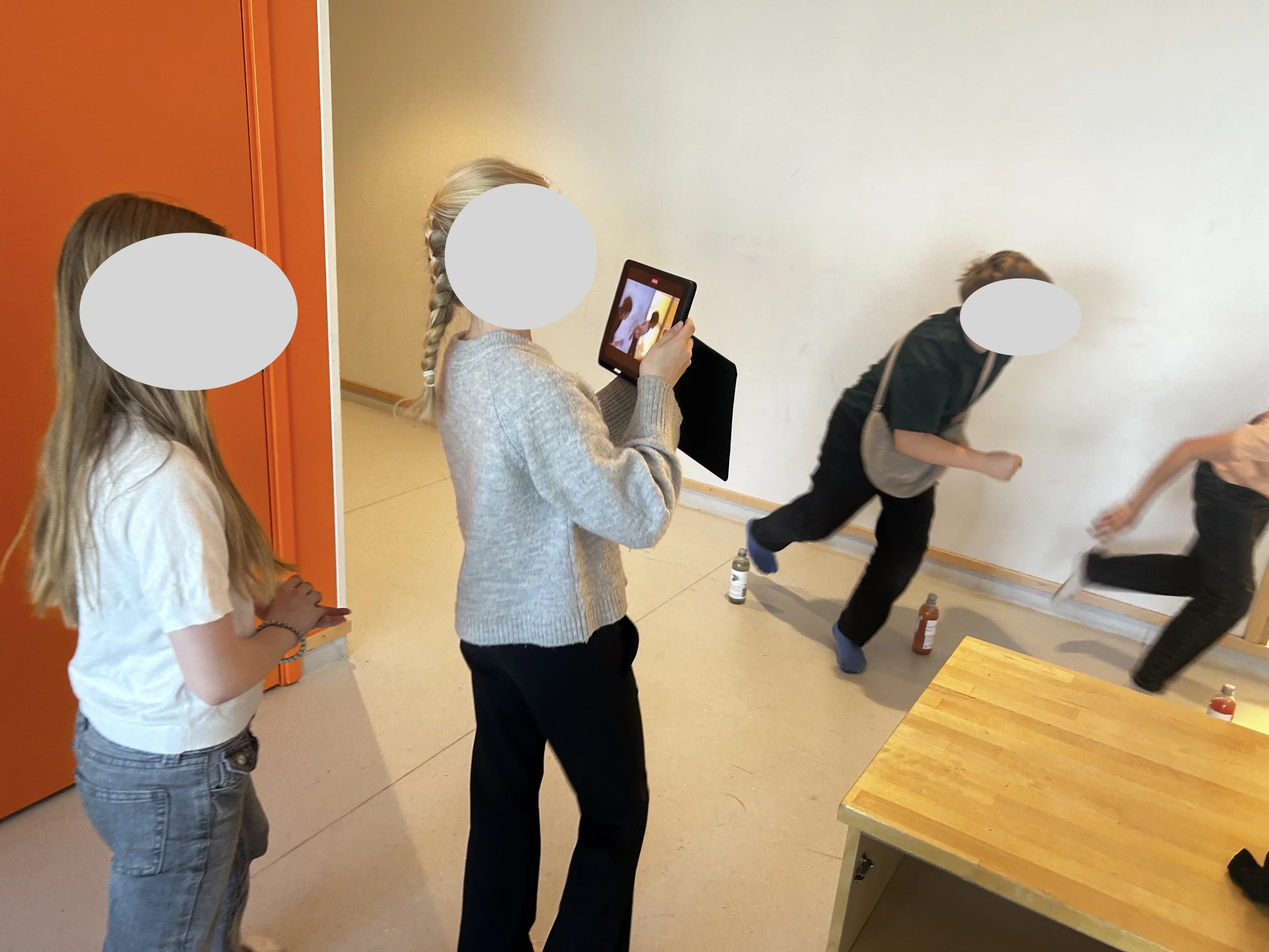 Flera personer står i ett rum, en person tar en bild med en surfplatta. Några personer är i rörelse, andra står stilla.