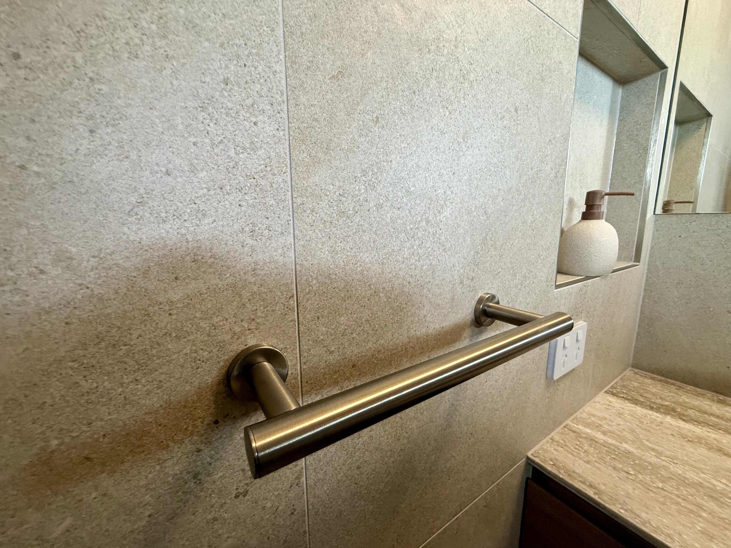 Brushed nickel hand towel rail beside tiled niche