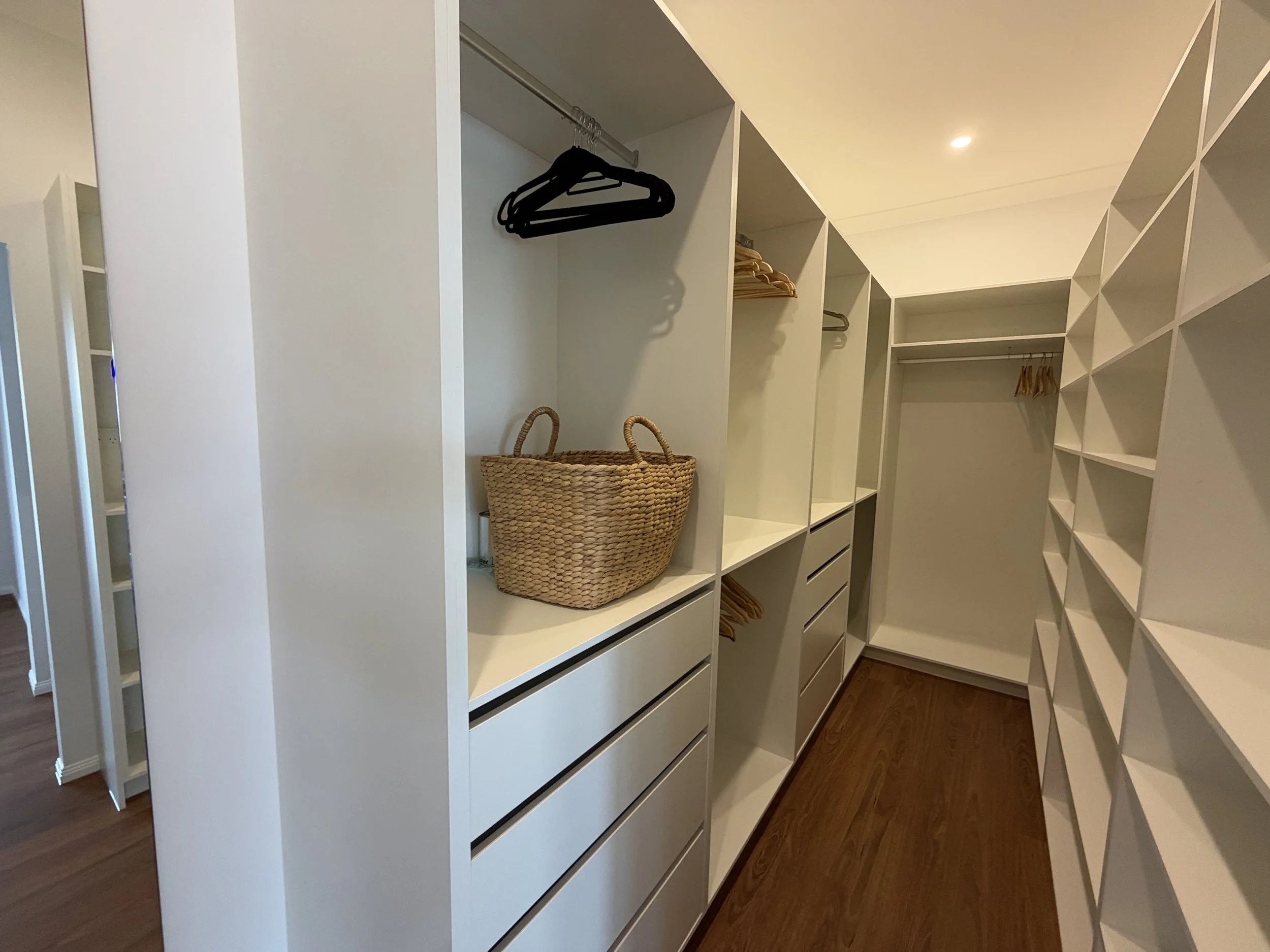 Custom walk-in wardrobe renovation in Wellington Point featuring white cabinetry, hanging space, drawers and open shelving.