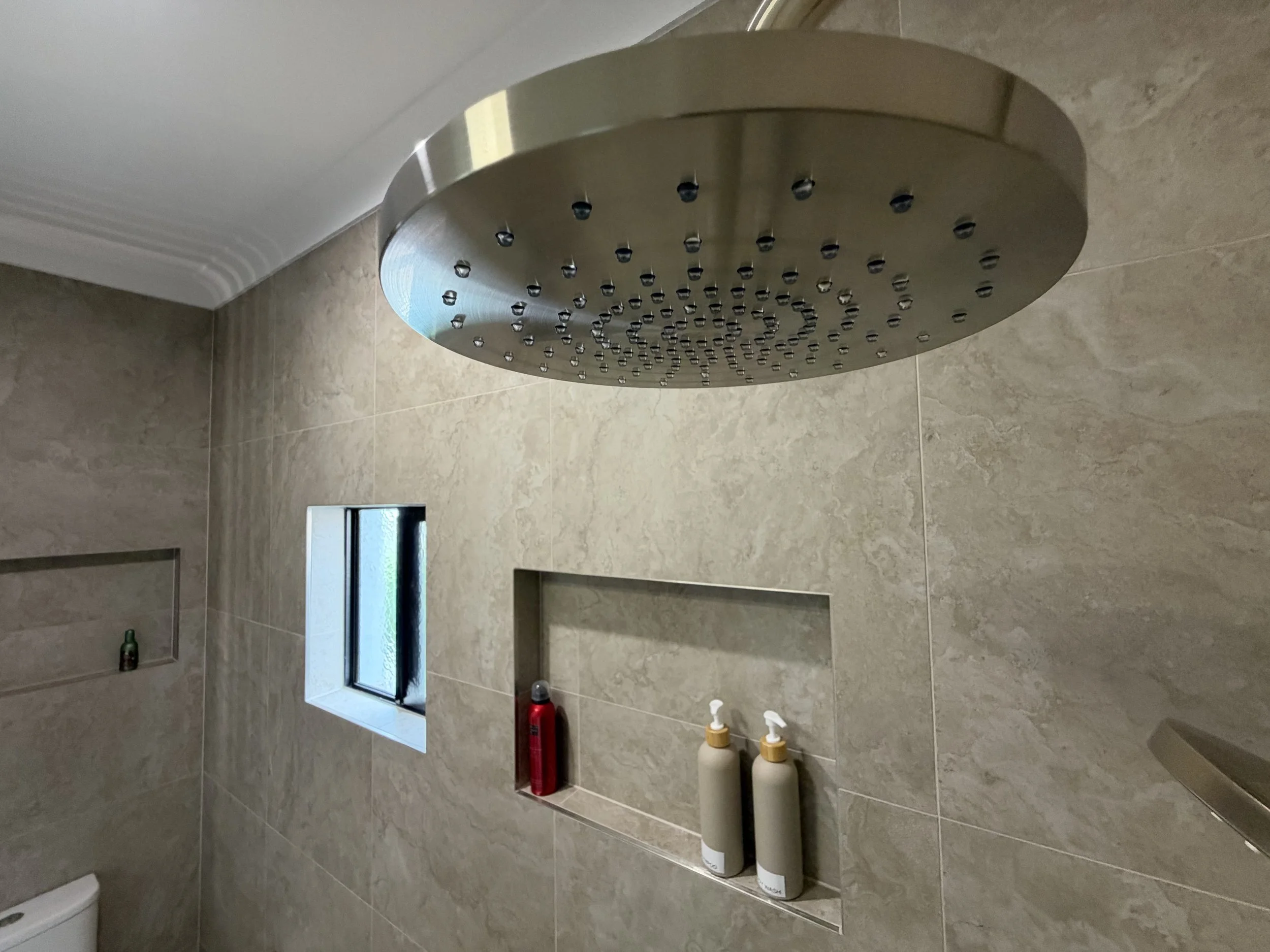 Luxury bathroom renovation featuring a tiled shower niche with brushed nickel fittings and large-format stone-look wall tiles.