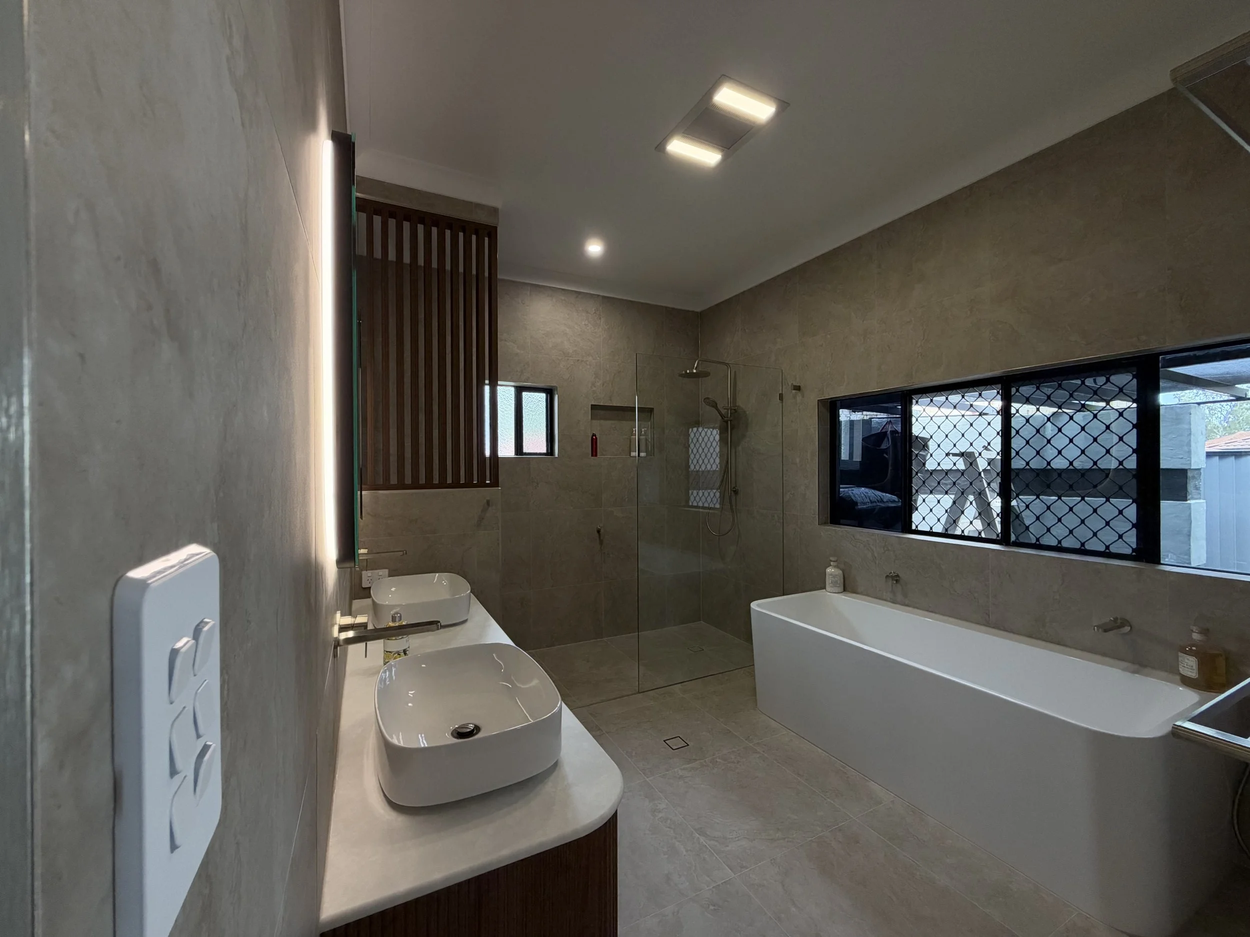 Contemporary bathroom renovation featuring large-format Lucca Crosscut Natural tiles, freestanding bathtub and frameless glass shower.