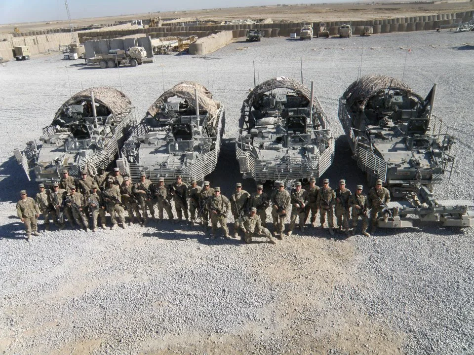Group of soldiers standing in front of armored military vehicles in a desert setting.