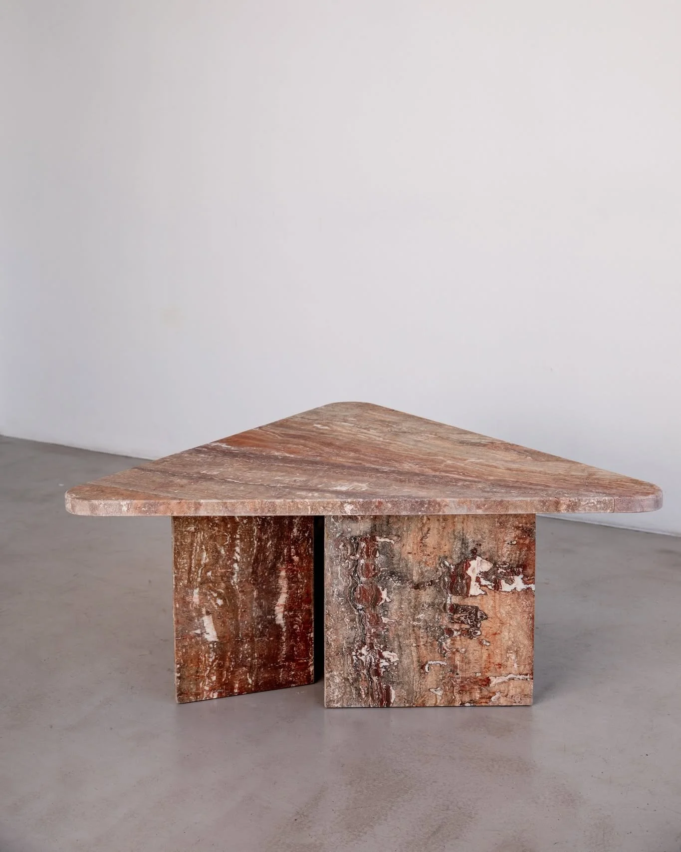 The triangular red travertine outdoor table.

Designed and crafted from natural stone offcuts, each piece carries traces of different decades, brought together into one timeless form.

The 1.3m top is made from two 30mm offcuts carefully joined as on