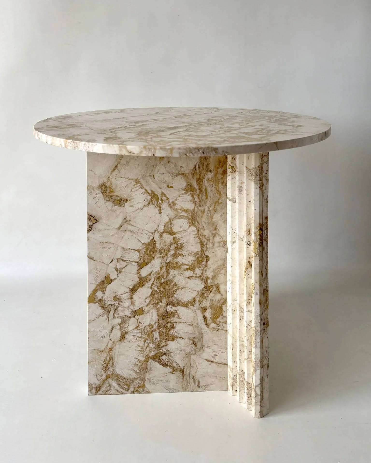 Rapolano travertine breakfast table - a bespoke design crafted from reclaimed offcuts of a rare travertine, reuse through material-led design. 
The vivid gold veining cuts through the warm white stone, while the overlapping structure is softened by a