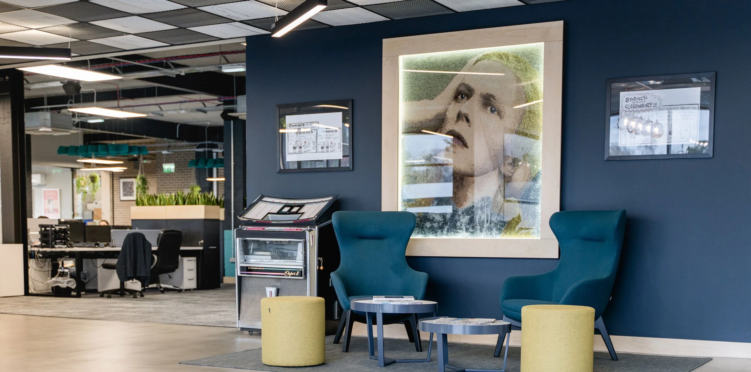 Modern accountants office reception area, two blue armchairs, two small round tables, and chairs. Large framed artwork and a retro juke box.