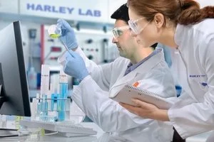 Two scientists in laboratory coats working with test tubes and a computer in a laboratory setting.