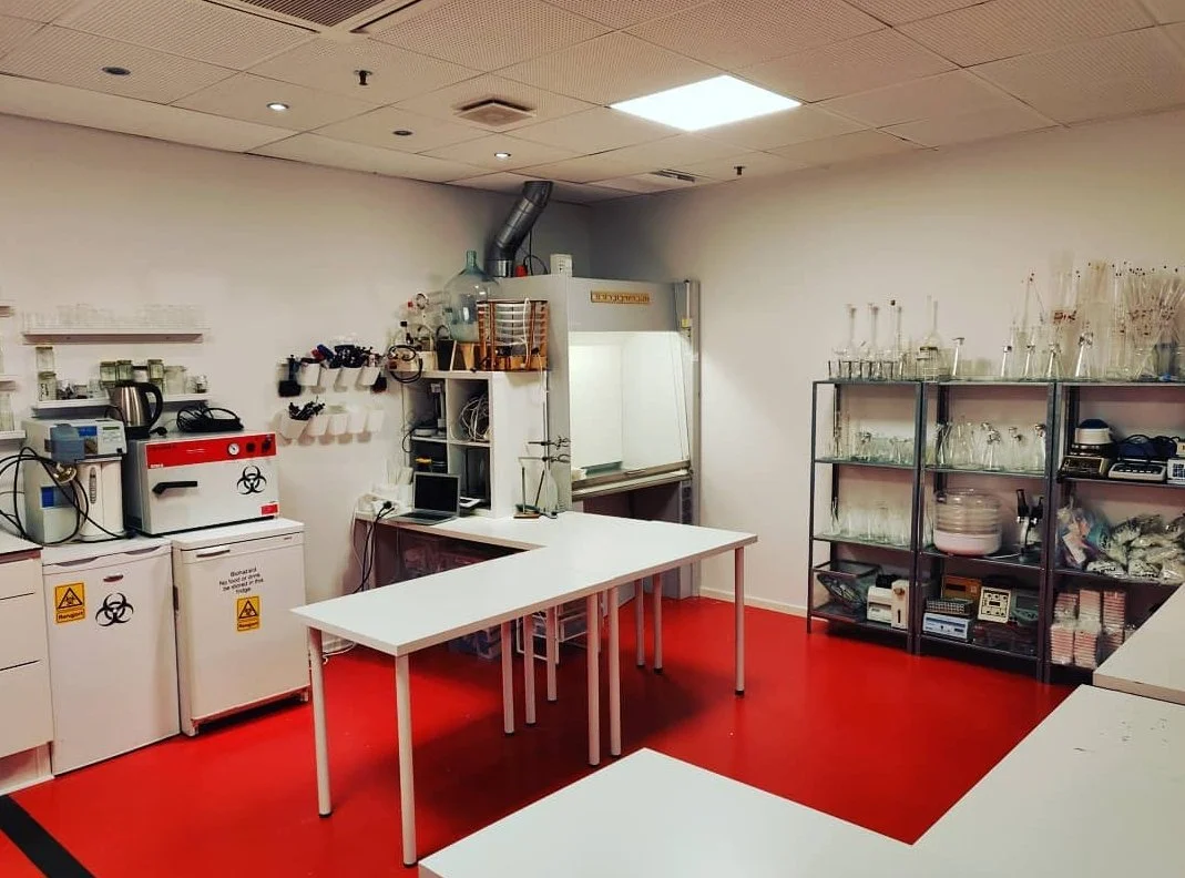 Chemical laboratory with safety signs on cabinets, lab equipment on shelves, and a fume hood against the wall.