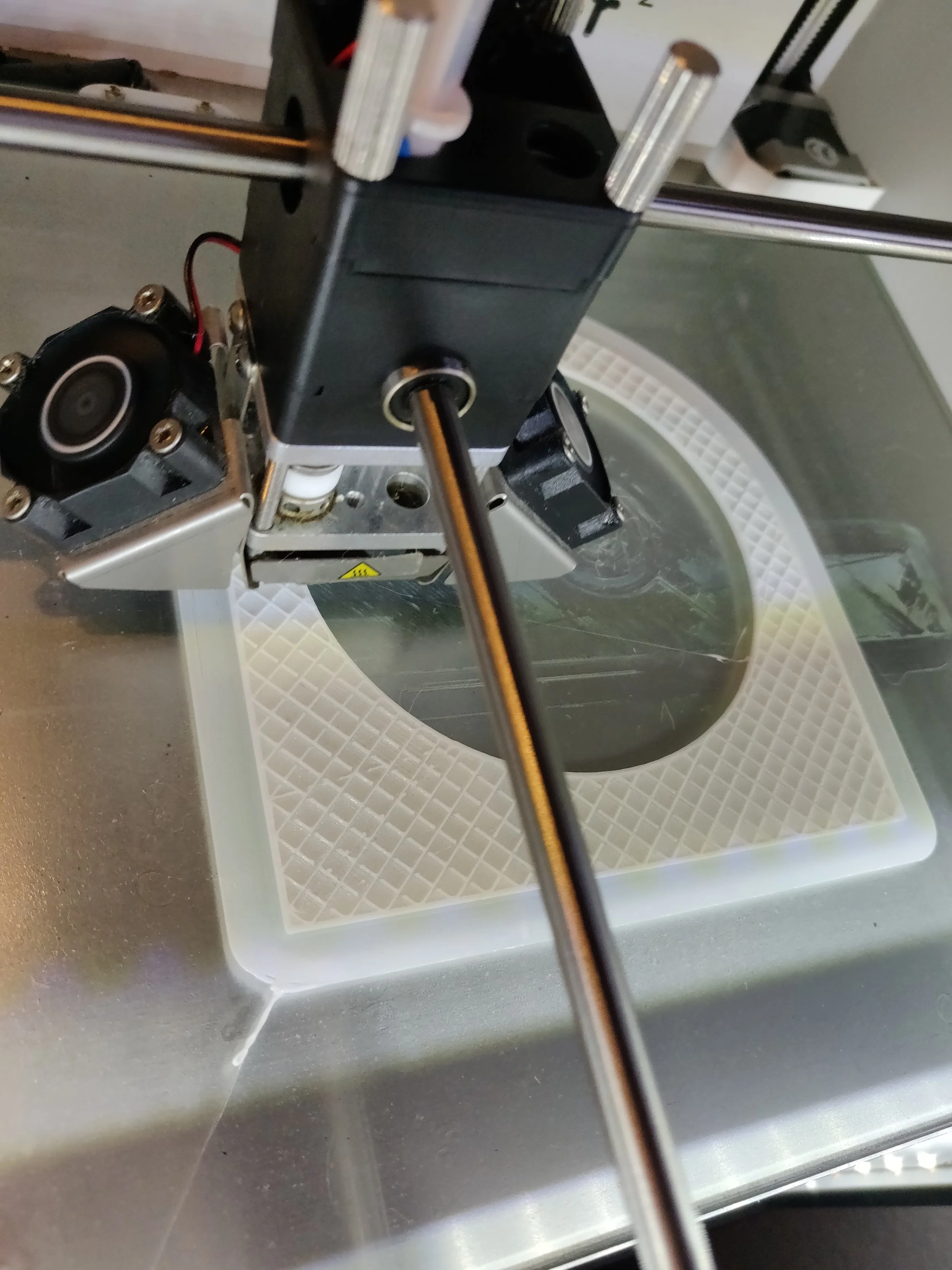 Close-up of a 3D printer nozzle connected to a black metal frame with a white textured print bed underneath.