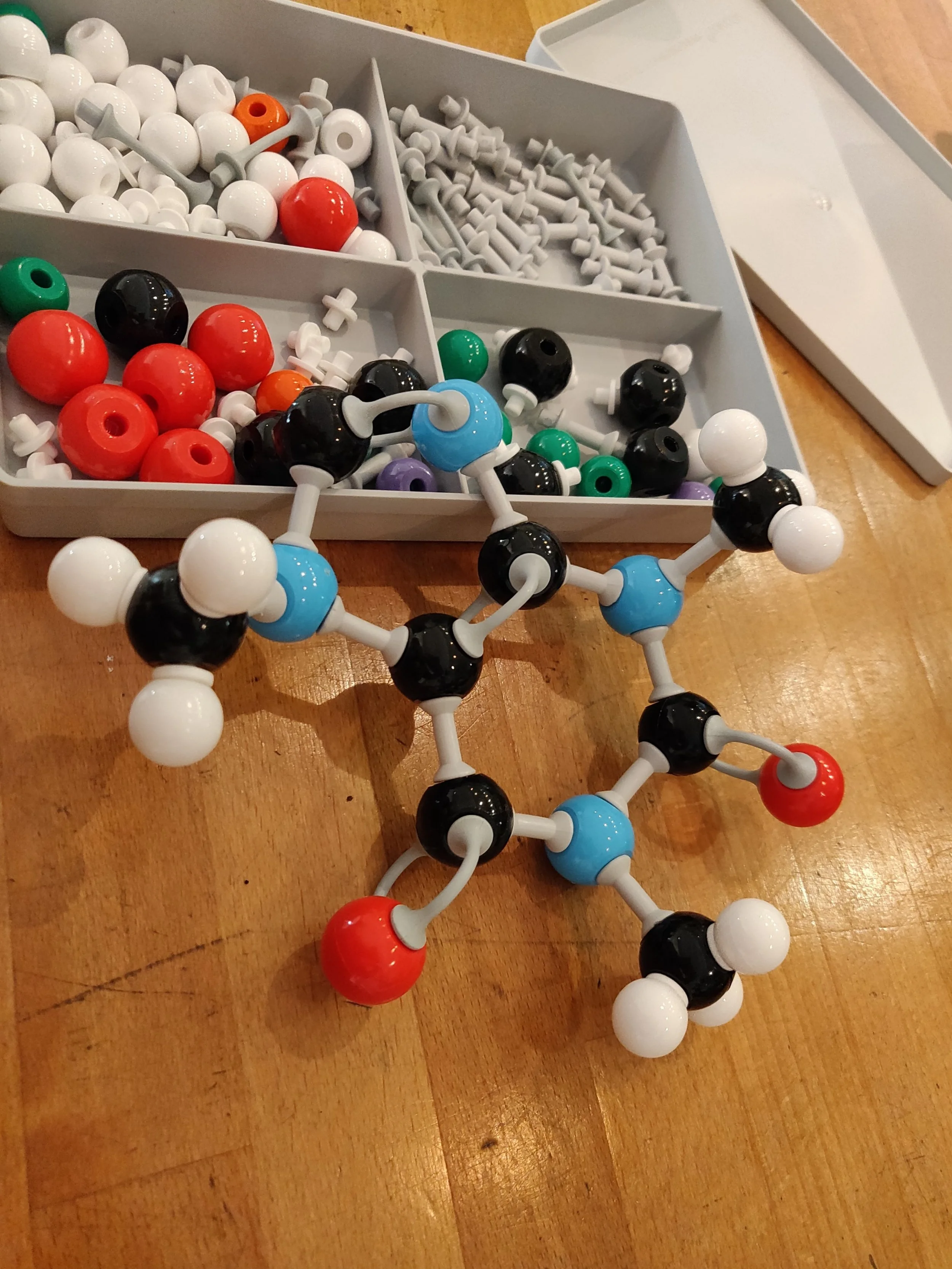 A molecular model on a wooden surface with a plastic container of various colored BeadStyle pieces in the background.