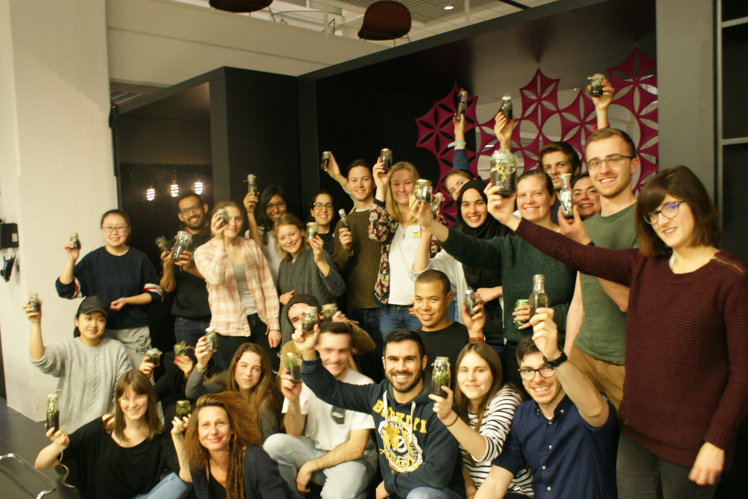 Group of smiling people indoors, holding bottles, celebrating or enjoying a gathering.