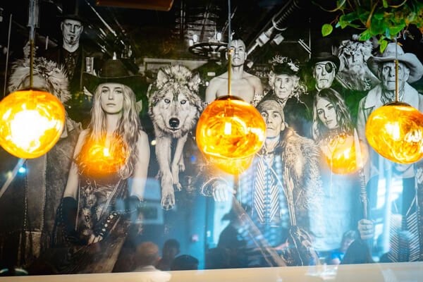 Black-and-white wall art in the restaurant with various characters in costume and a wolf, illuminated by three hanging lights.