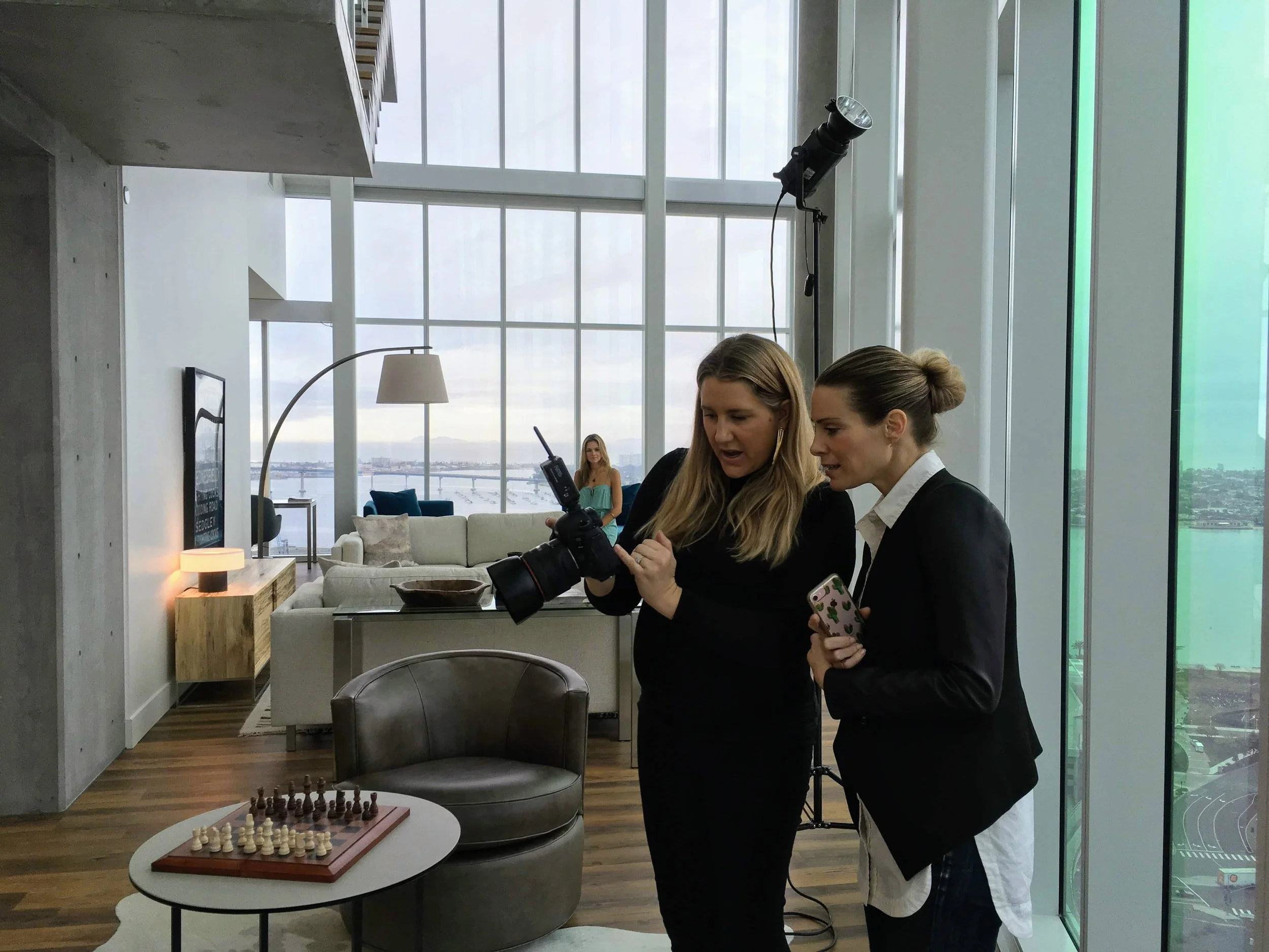 Photographer and magazine editor reviewing a photo taken of a model who sits behind them in a beautiful, high rise building.