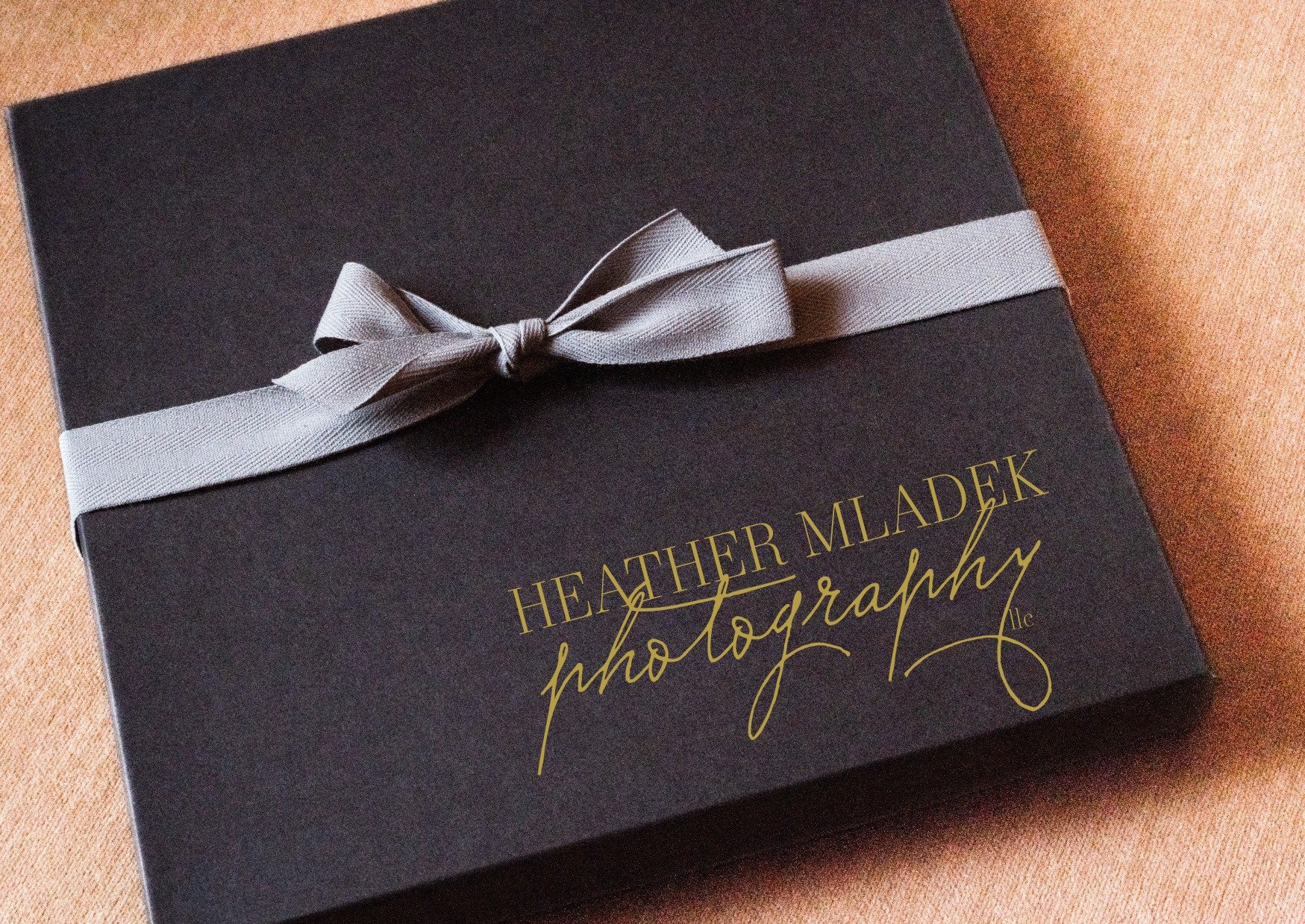 A photo of a black box tied with a light gray ribbon. A gift from Heather Mladek Photography. Perhaps holding a portrait album or a piece of wall art.