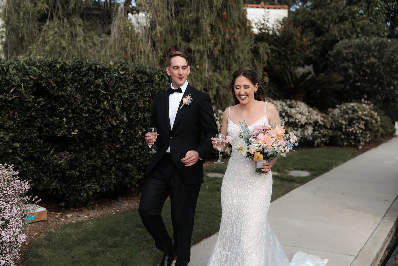 Canid photo of a bride and groom smiling while walking with a drink in hand at Thursday Club for their wedding in San Diego.