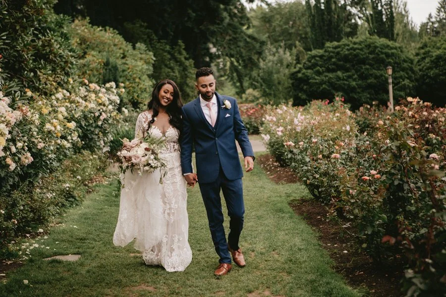 Bride and groom walk in a rose garden. 