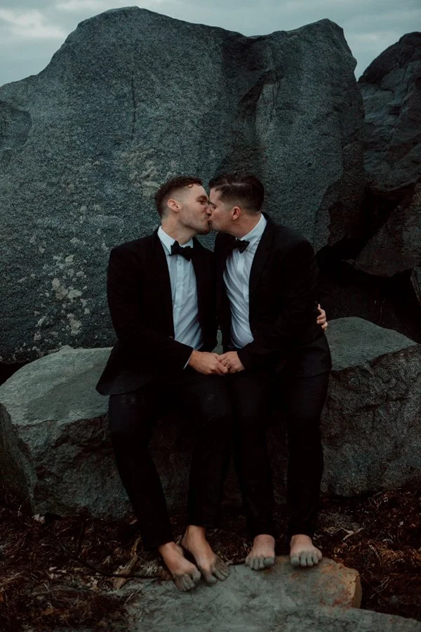Grooms kiss on rocks in San Diego.