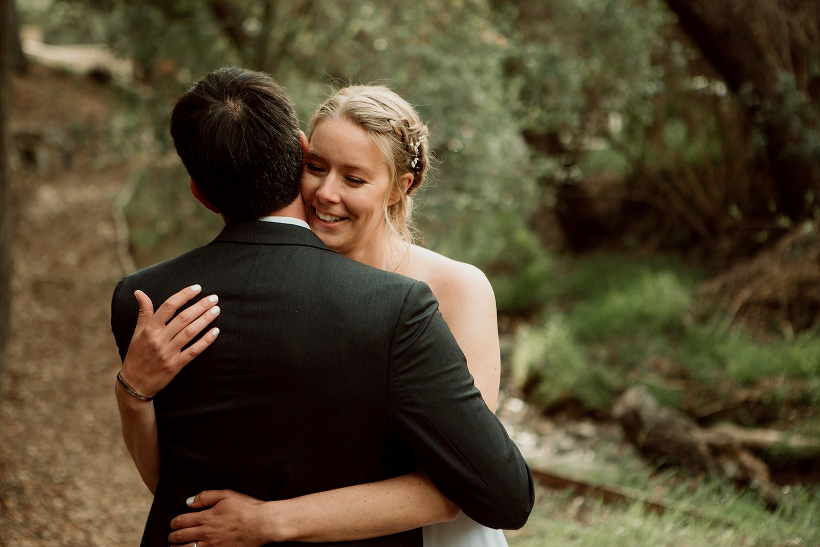 Bride hugs groom in a lush green path at their San Diego wedding.