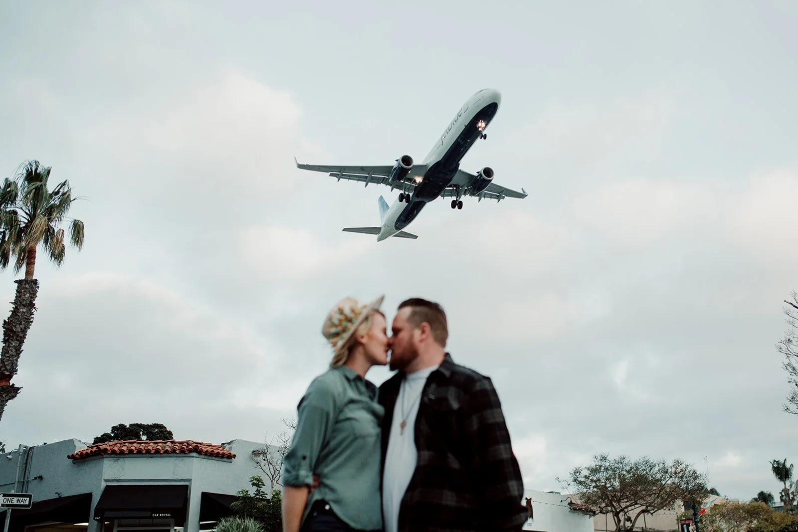San Diego engagement photo session a couple is kissing with a plane flying over.