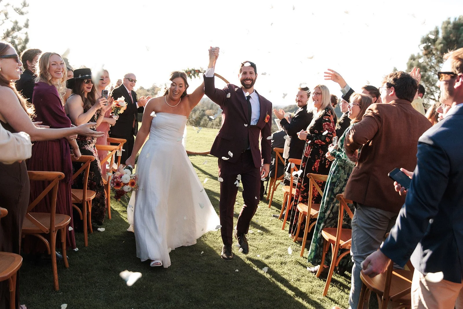 Bride and groom cheer as they walk away from their wedding ceremony while guests clap and smile.