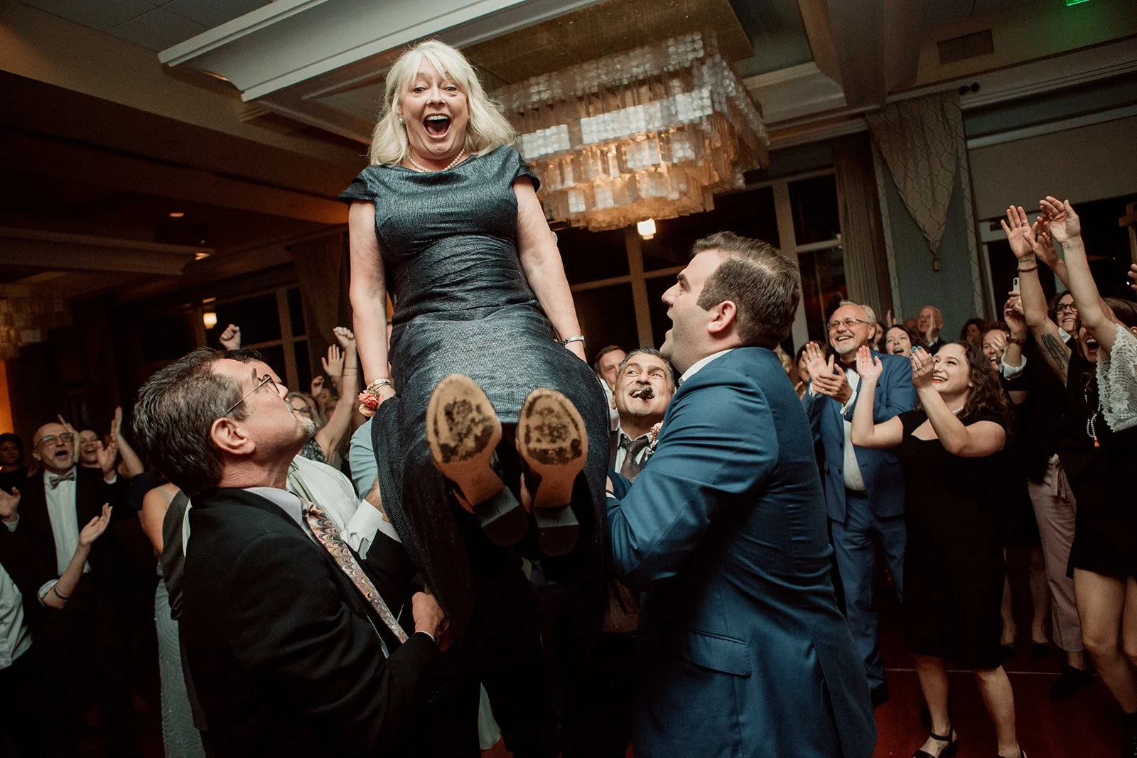 Woman gets lifted on chair during the hora at a San Diego wedding reception at Paradise Point.