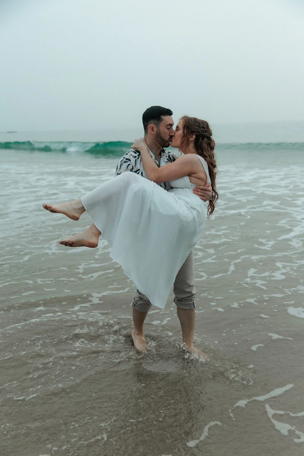 Man picks up his bride to be in the ocean for their San Diego engagement photos.