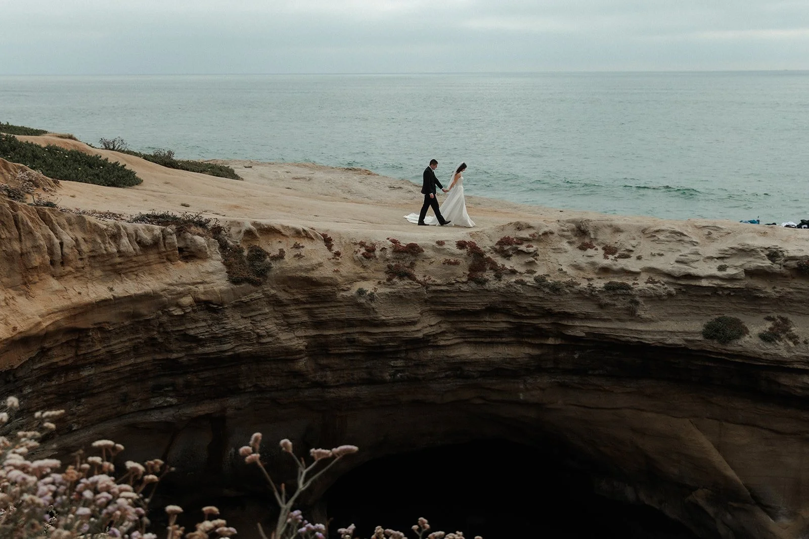 Bride and groom walking across a scenic overlook at Sunset Cliffs in San Diego, CA.