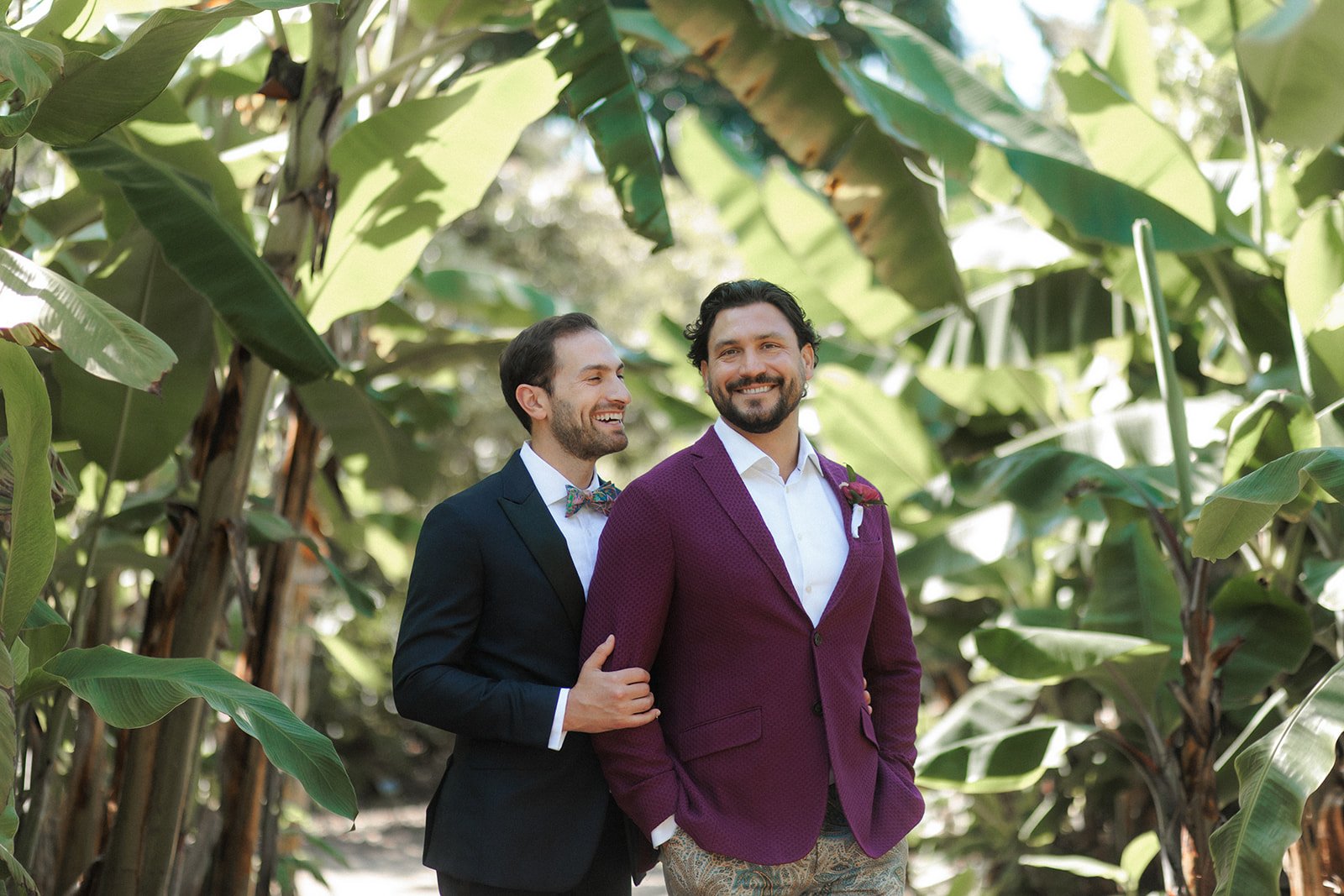 Two grooms embrace and smile at their San Diego wedding in Encinitas gardens.