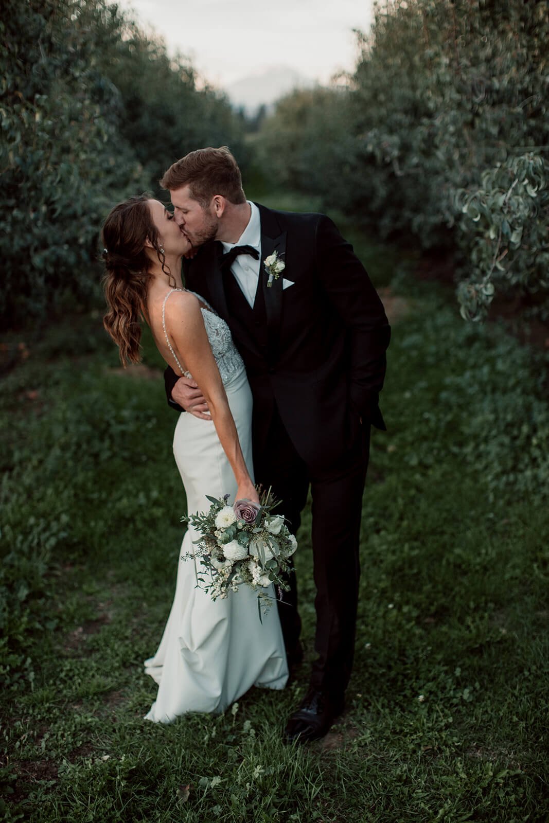 San Diego wedding photo of a groom kissing his bride in an orchard.
