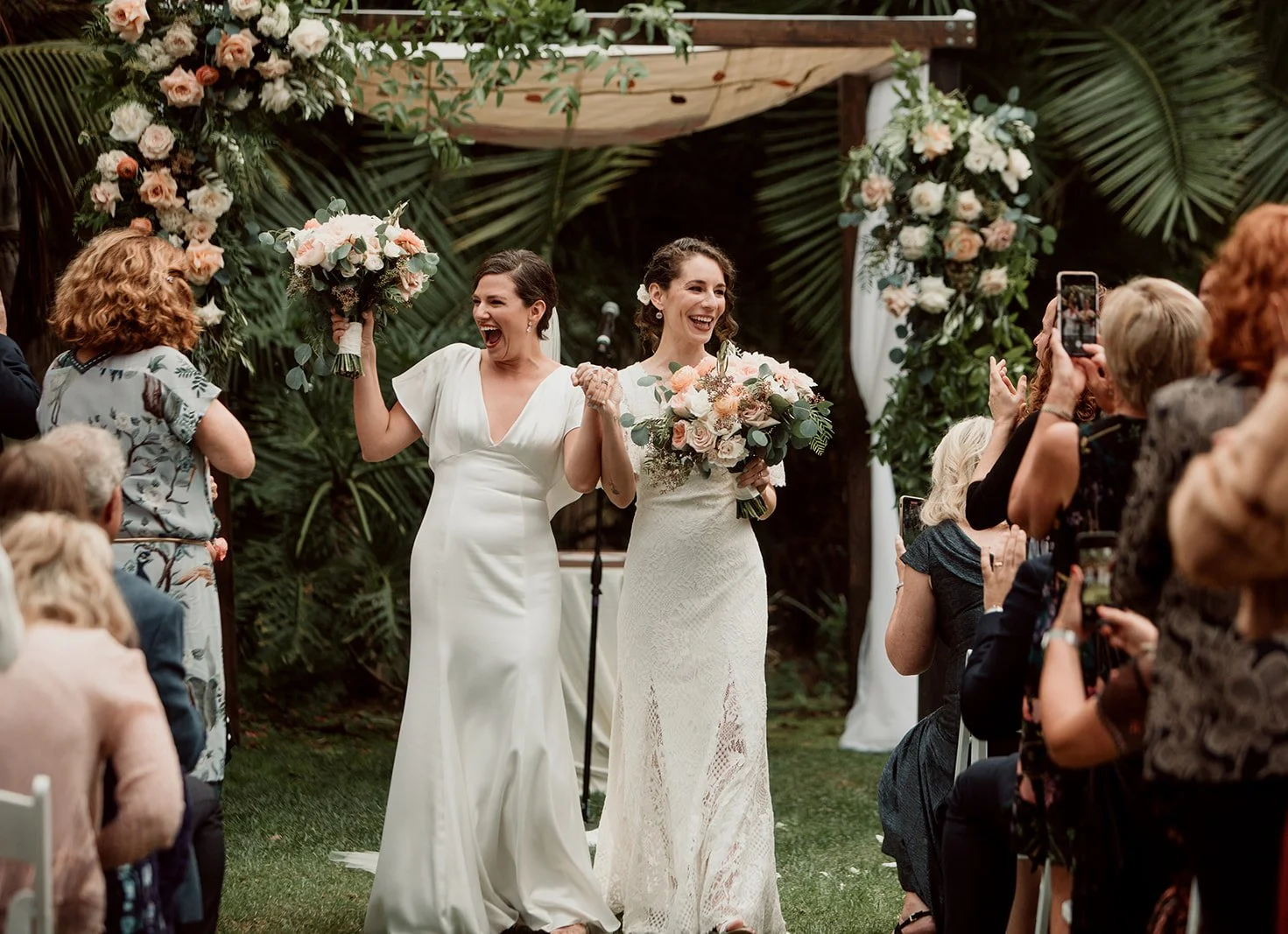 Brides walk down the isle while guests cheer at their Paradise Point wedding on San Diego Mission Bay.