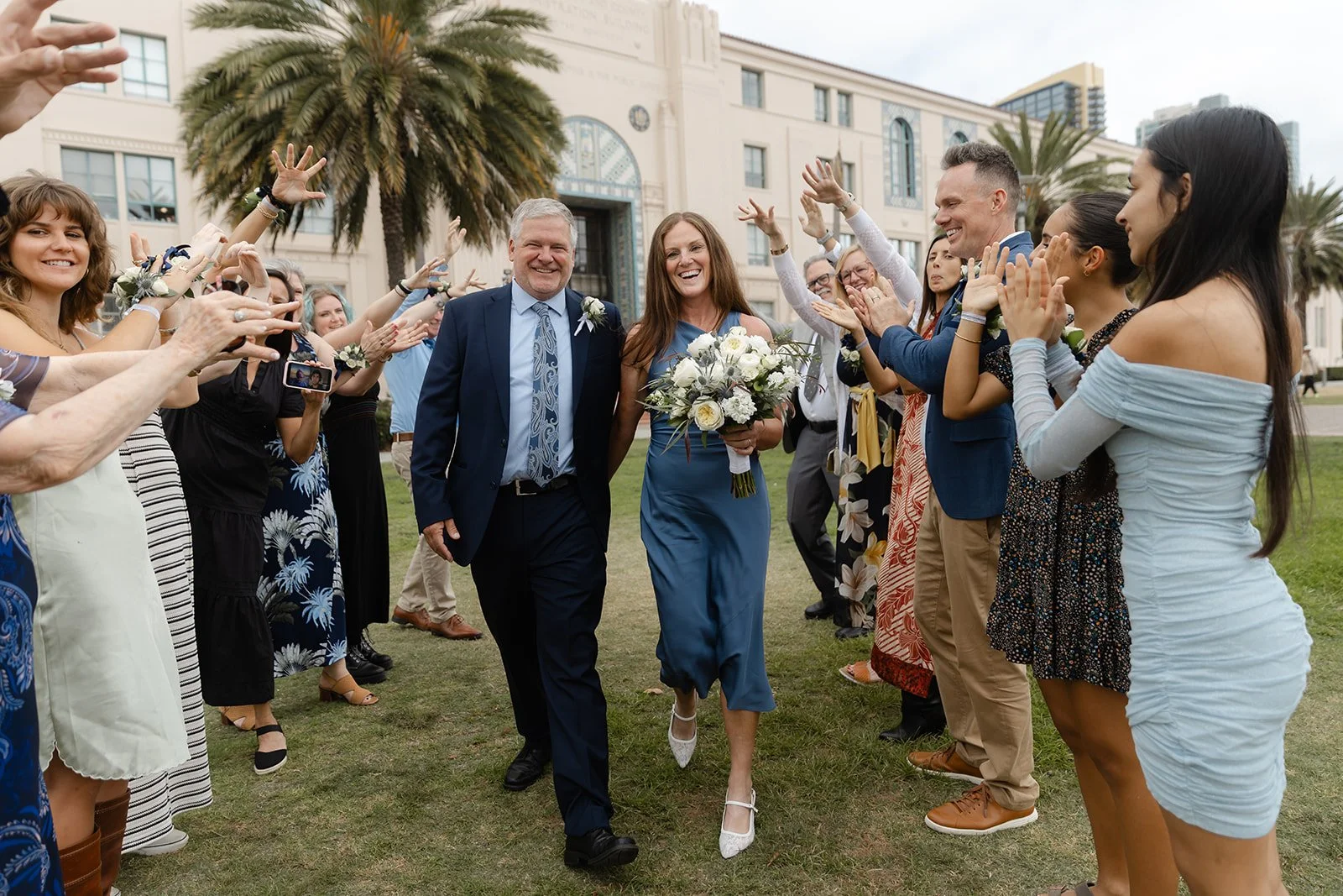 Couple laughs while walking past their guests that are clapping at the San Diego courthouse.