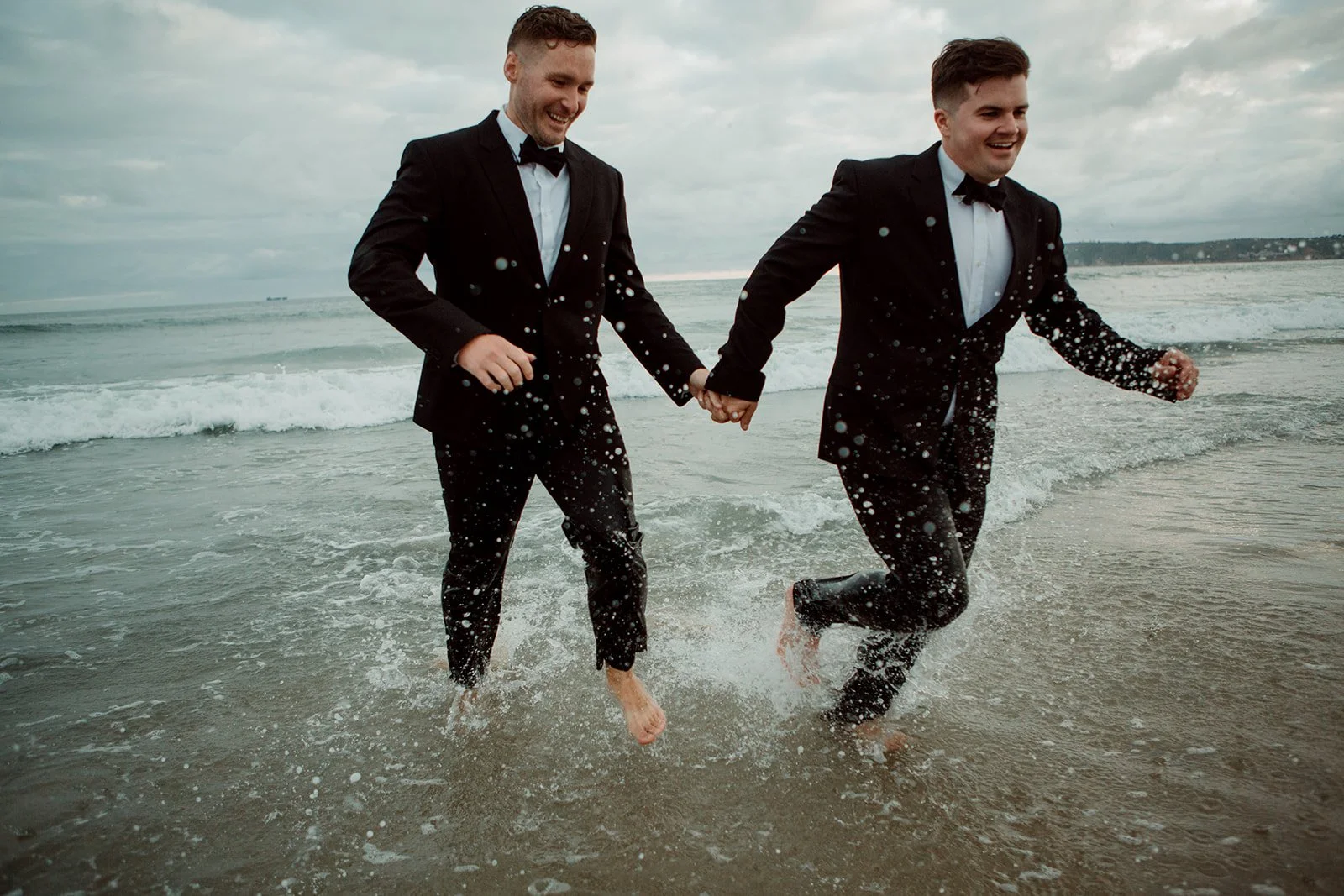 Two grooms hold hands and smile for their San Diego elopement on Coronado Beach.