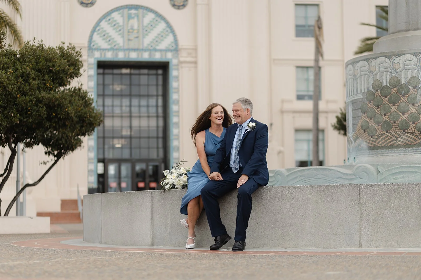 Couples sits on fountain in front of San Diego Administrative Building after their courthouse ceremony.