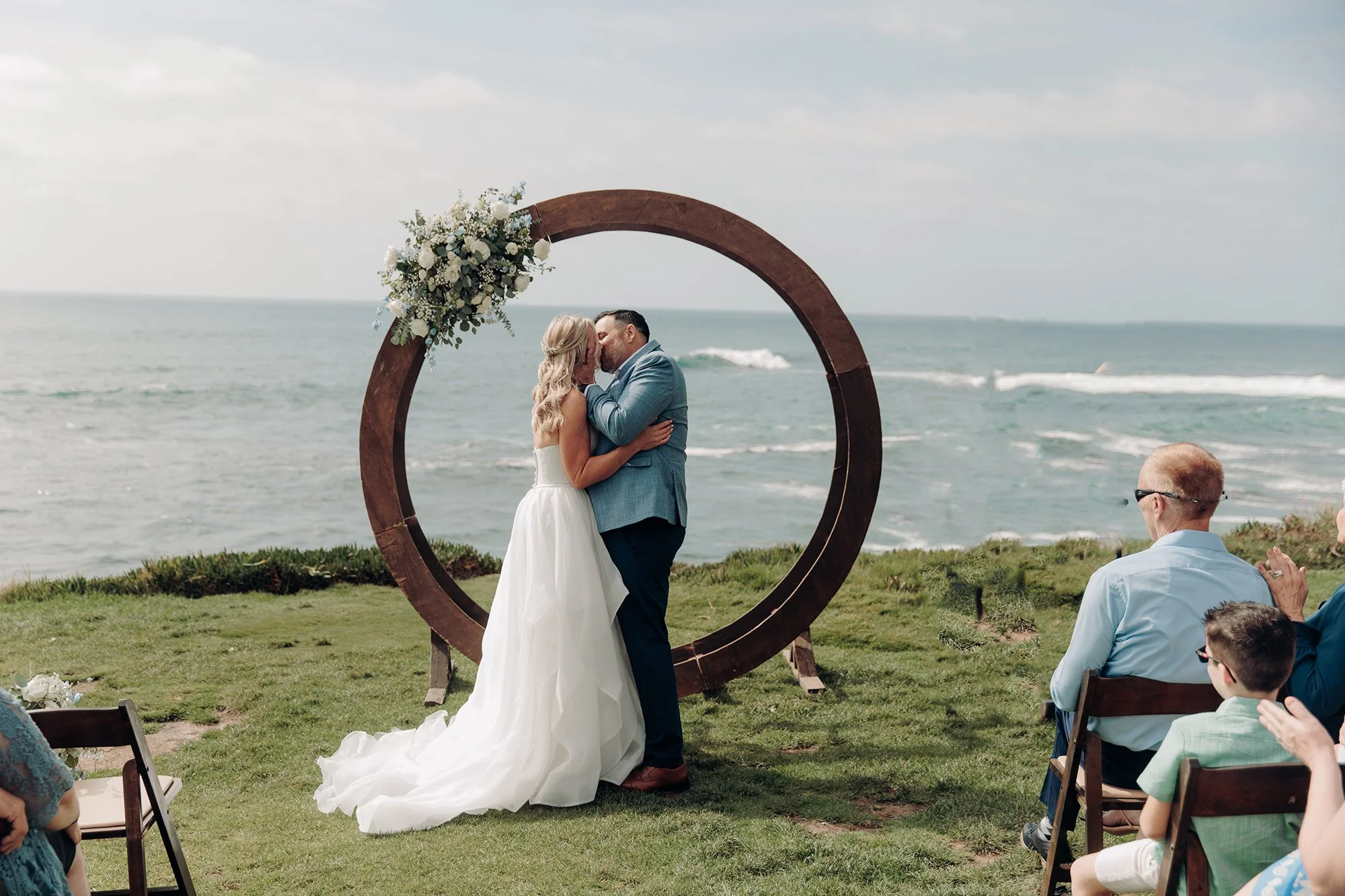 San Diego beach wedding photograph of groom kissing bride in front of ocean.  Indigo West Photography. Award winning San Diego wedding photographer.