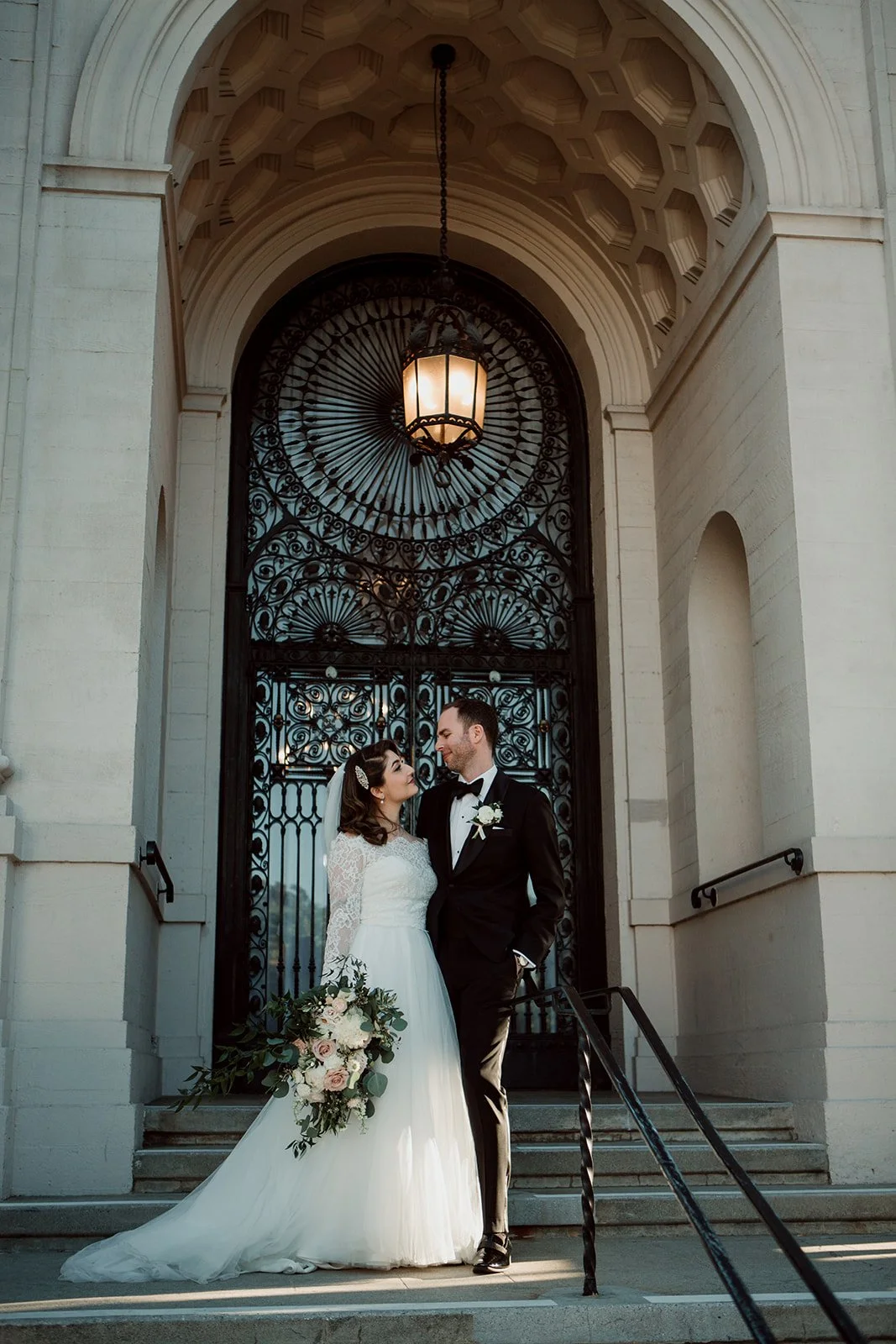 Bride and groom stand embracing in front of a beautiful building in Los Angeles. 