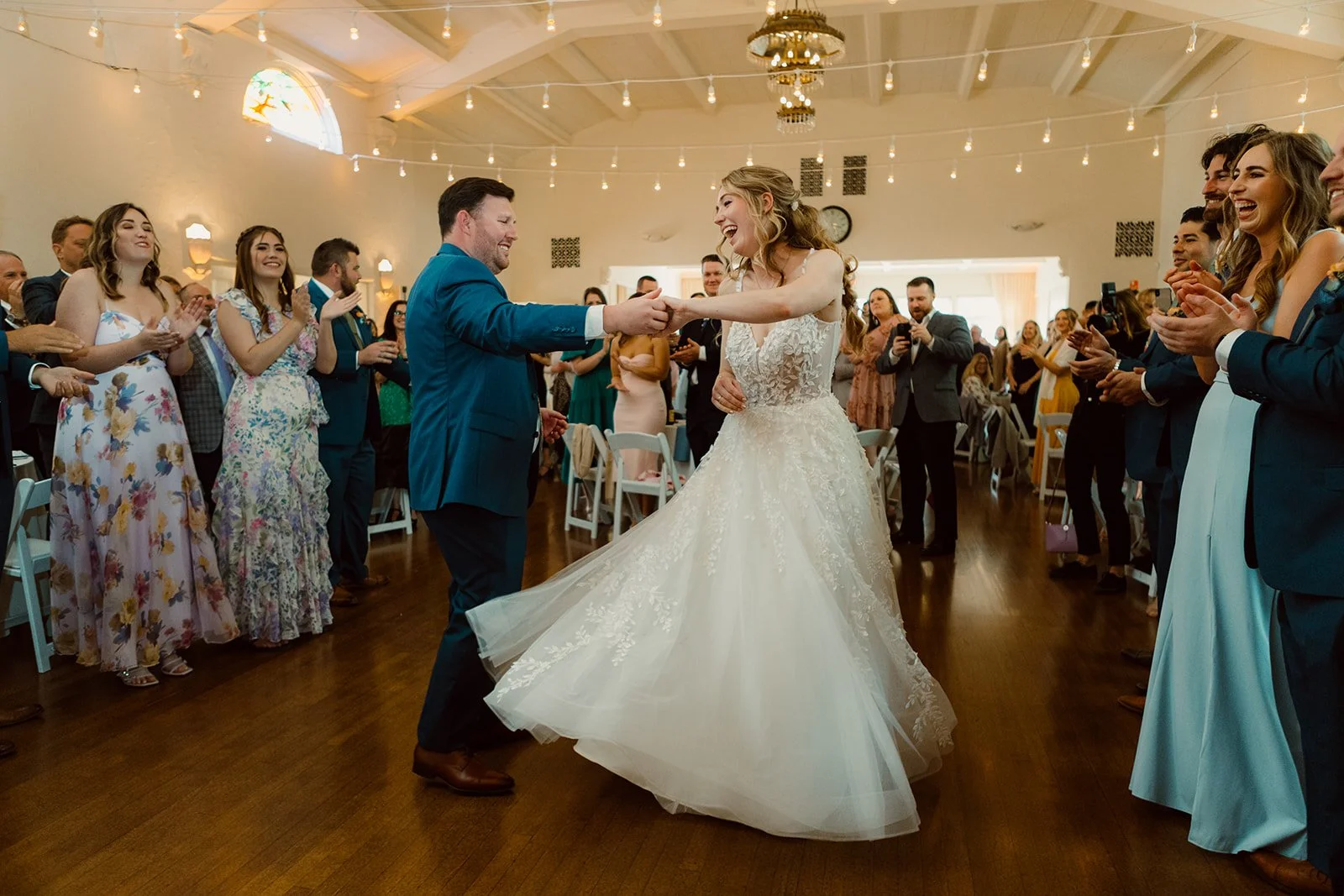 Grand entrance at a San Diego wedding held at Thursday Club in Point Loma. Groom twirls his bride while she laughs and guests stand clapping.
