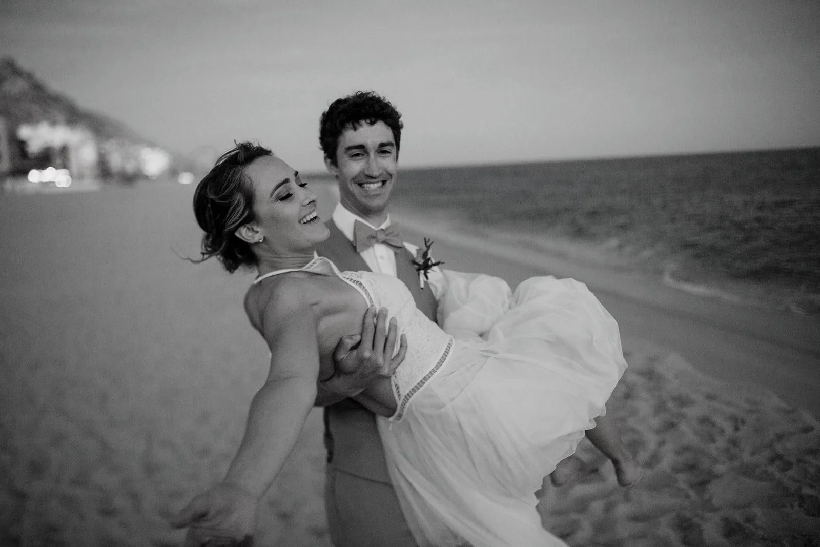 Groom picks up his bride on a San Diego beach for their sunset photos.