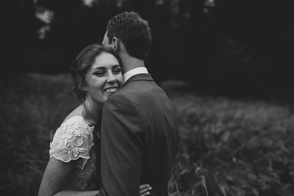 Bride in a field hugs her groom and smiles at their San Diego wedding. 
