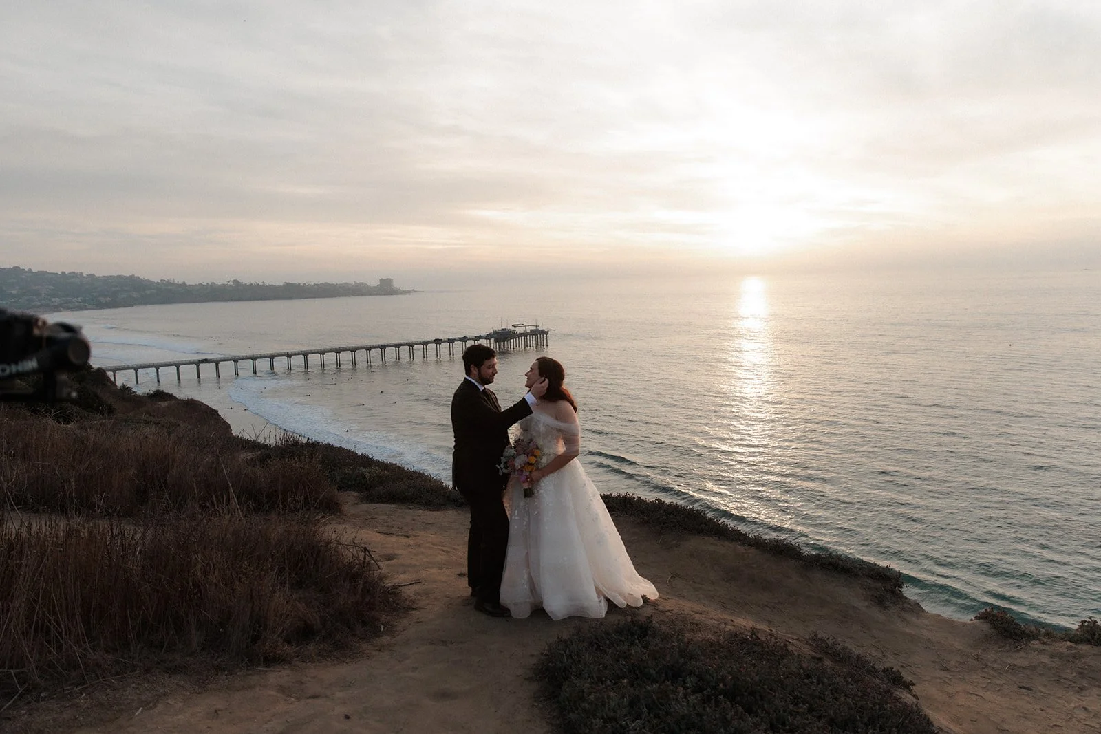 Couple shares a candid moment on a scenic overlook at sunset their during San Diego beach coastal wedding at The Martin Johnson House.