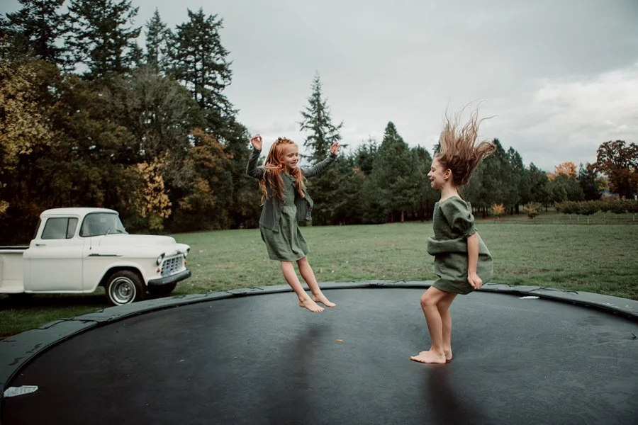 Two flower girls joyfully jump on a trampoline at a San Diego wedding.