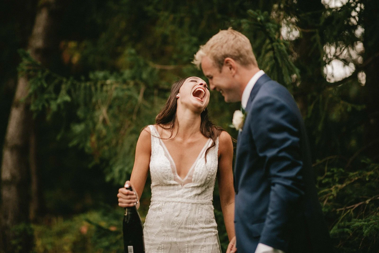 Bride laughs holding a champagne bottle at her San Diego wedding reception.