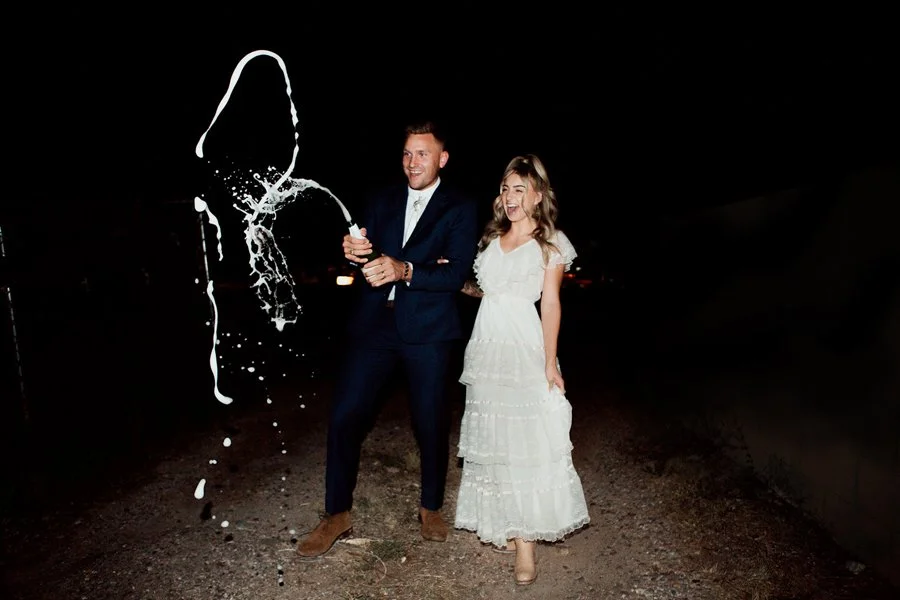 Couple pops a bottle of champagne at their San Diego wedding reception.