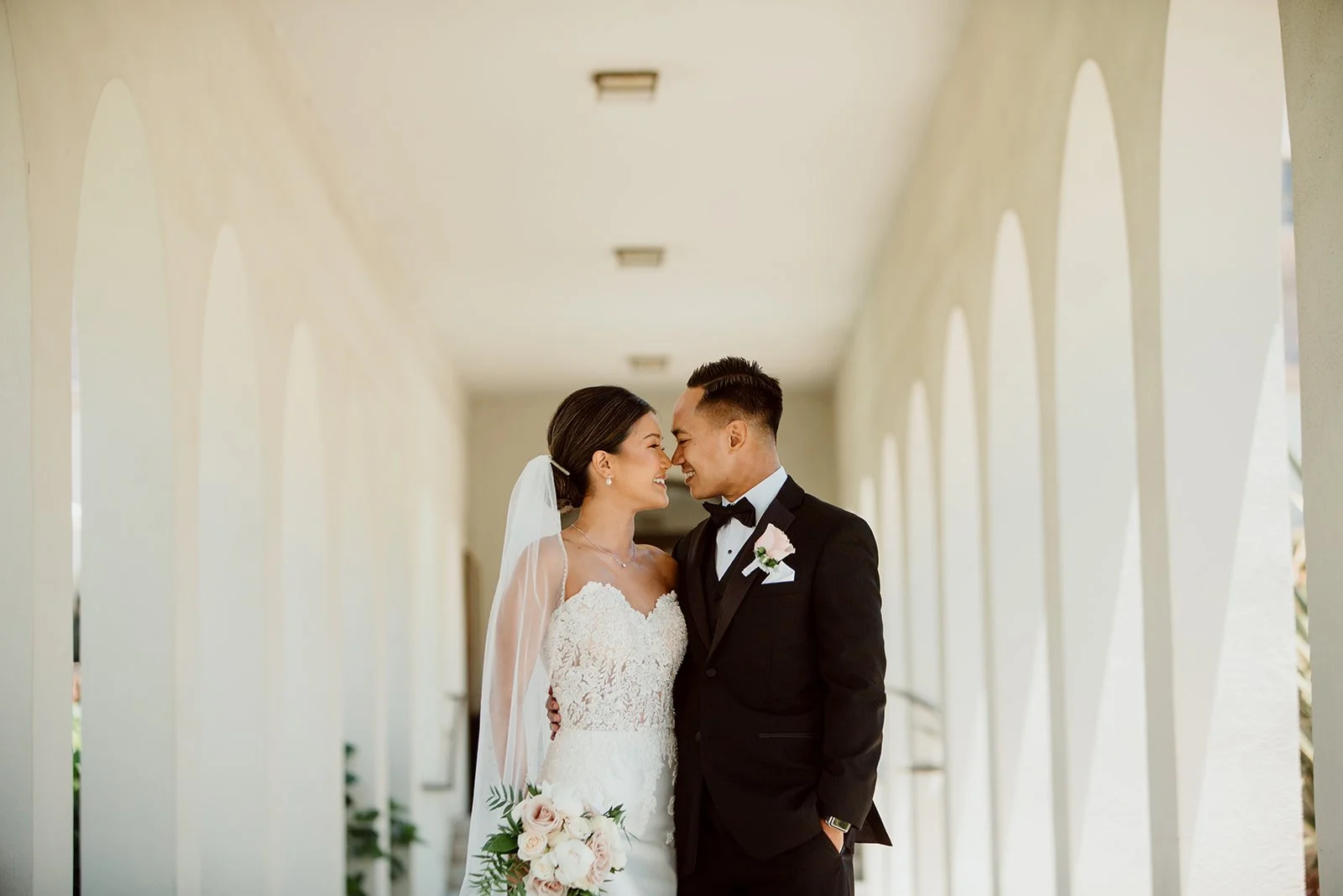San Diego couple embraces and smiles under old Spanish Colonial arches.