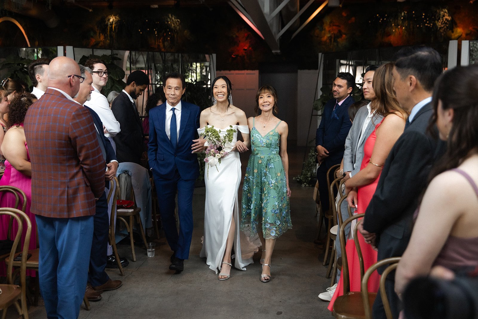Bride walks to her wedding ceremony accompanied down the isle by her parents at Flora the Venue in San Diego.